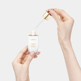 Two hands gently hold and dispense the Sulwhasoo Concentrated Ginseng Brightening Spot Ampoule, showcasing its elegant design and highlighting its ability to improve dull skin and dark spots.